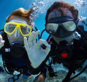 underwater shoot of a young couple diving with scuba in a tropical sea and showing ok signal shutterstock 127605290